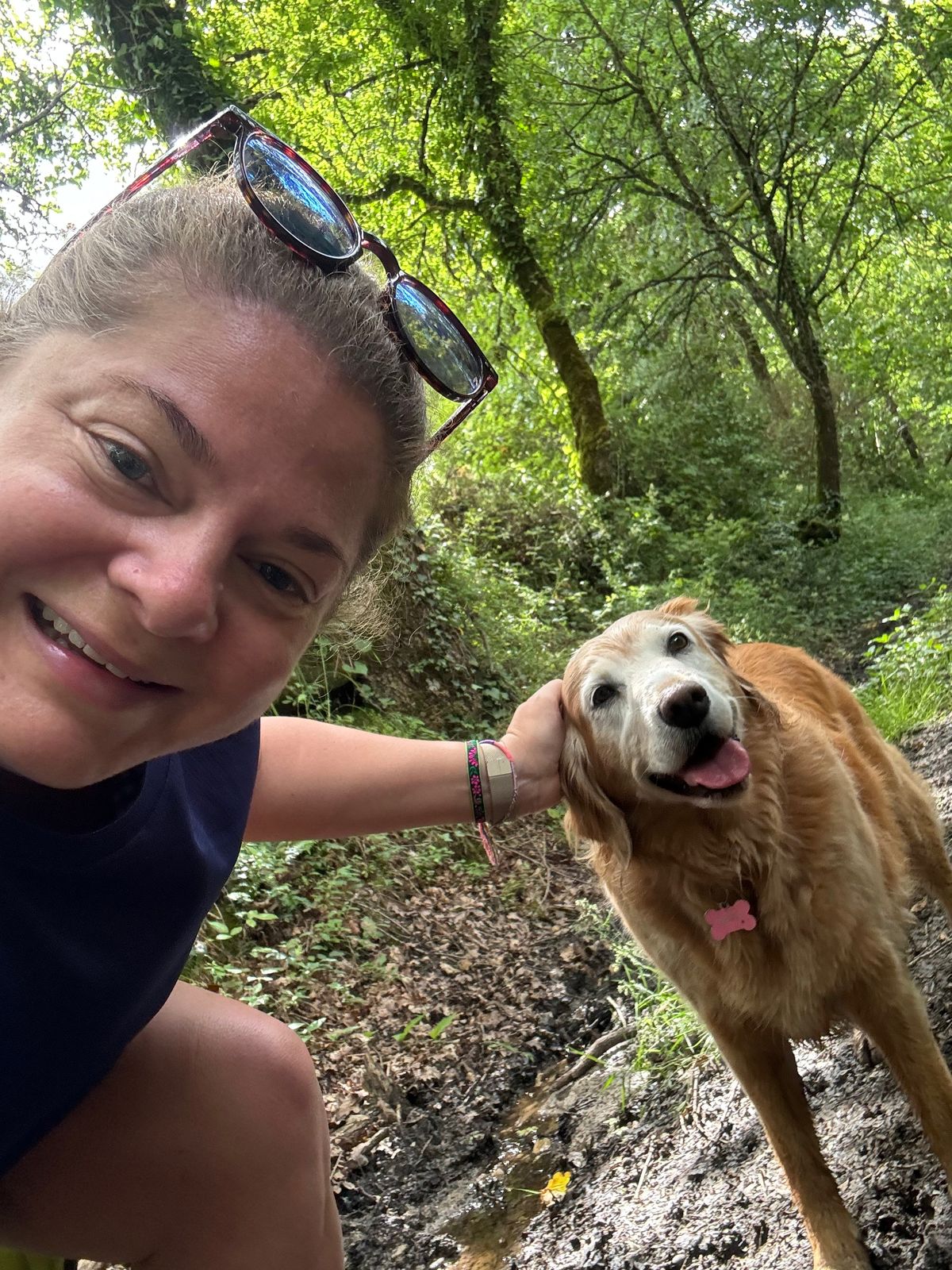 Cassie smiling beside a golden dog on a woodland path