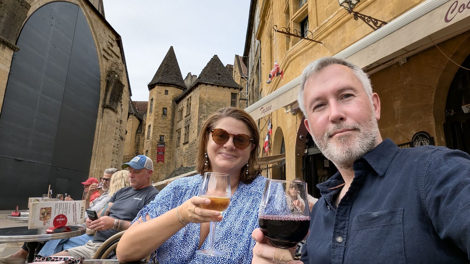 Kev and Cassie raising glasses of wine on a café terrace in Sarlat