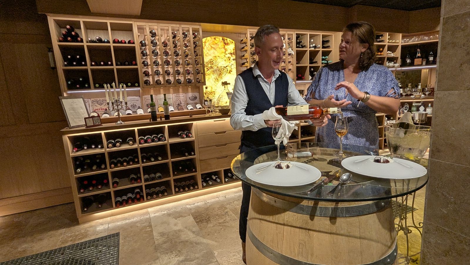 Patrick, in a waistcoat and white gloves, serving Cassie a small dish at the tasting table at Aux 3 Sens