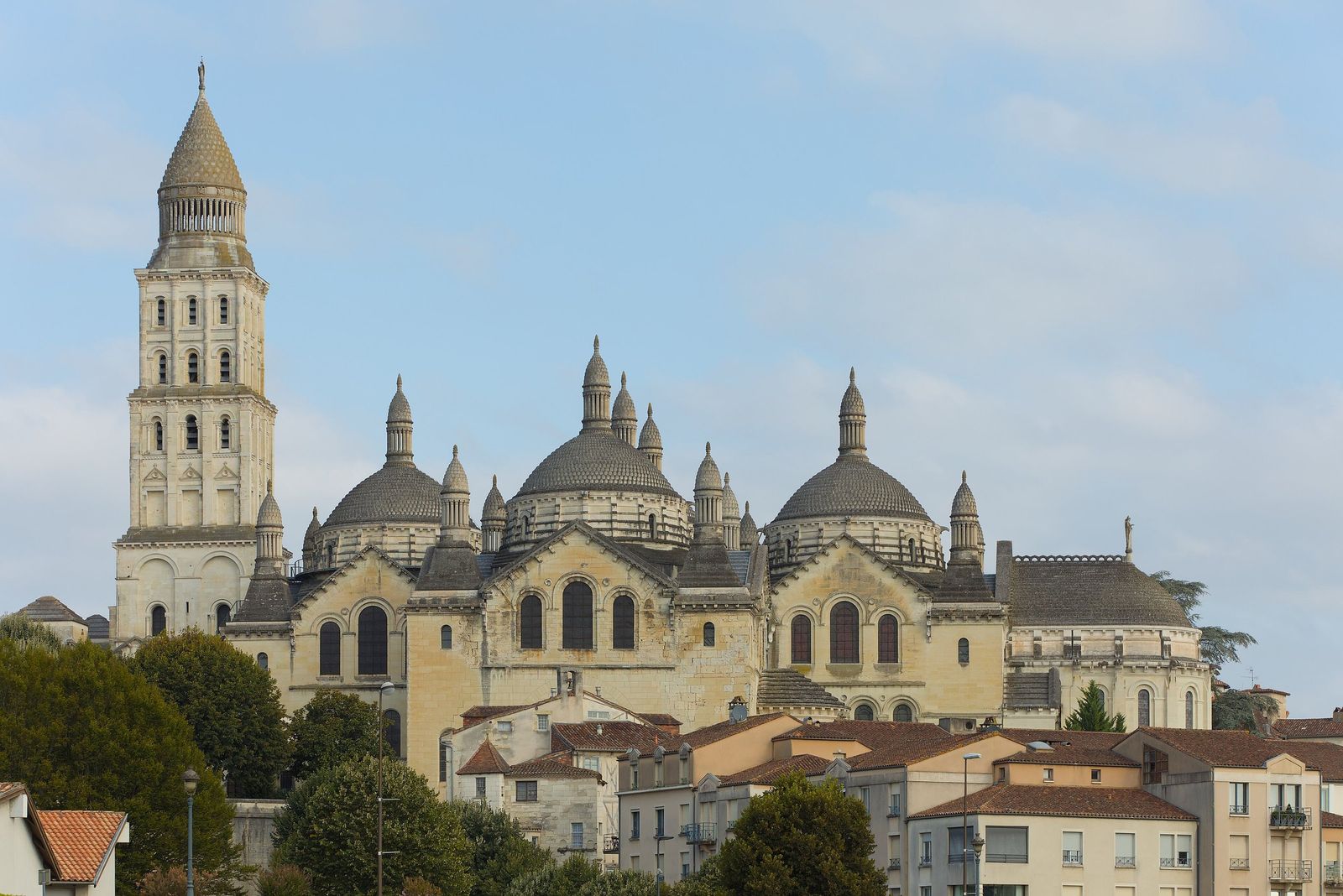 Périgueux's Cathédrale Saint-Front rising above the town's roofs, with its tall bell tower, several grey domes topped by small pointed turrets and pale stone walls, under a soft blue sky.
