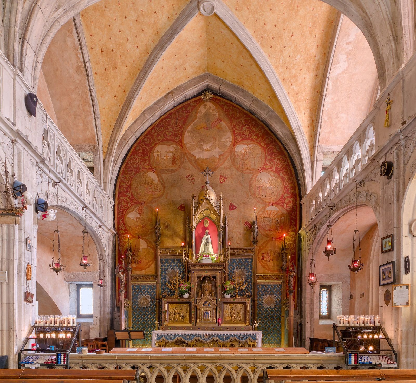 Inside Rocamadour's Chapelle Notre-Dame: a small dark statue of the Virgin and Child in a gilded shrine above the altar, set against a painted red arch, with candles and hanging lamps either side.