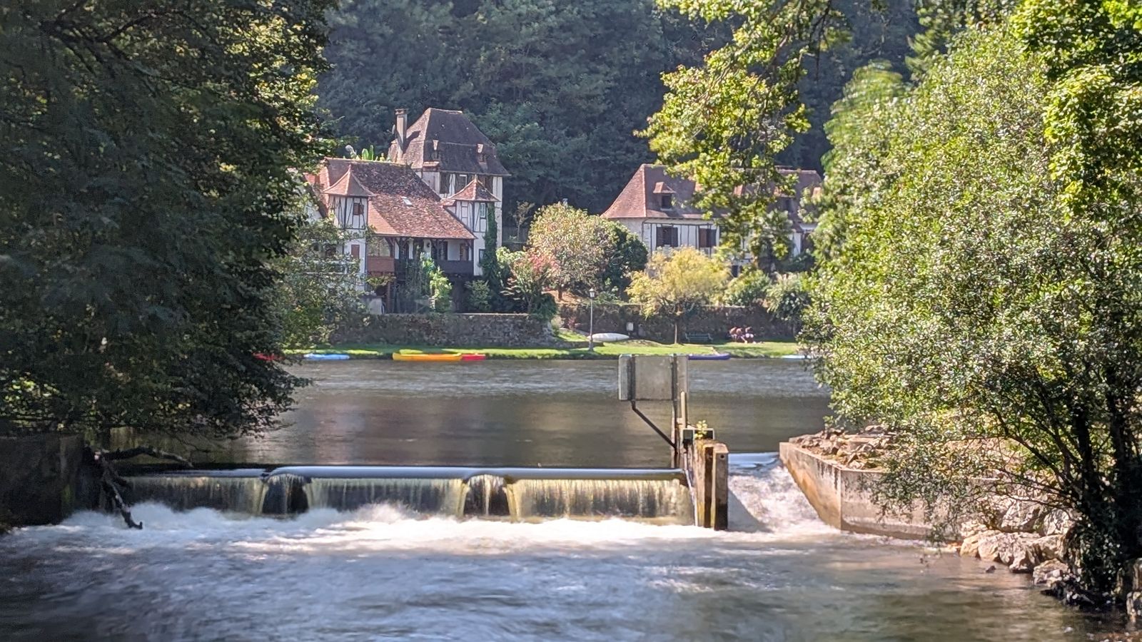 The Dordogne flowing over a weir at Beaulieu-sur-Dordogne, with houses among the trees