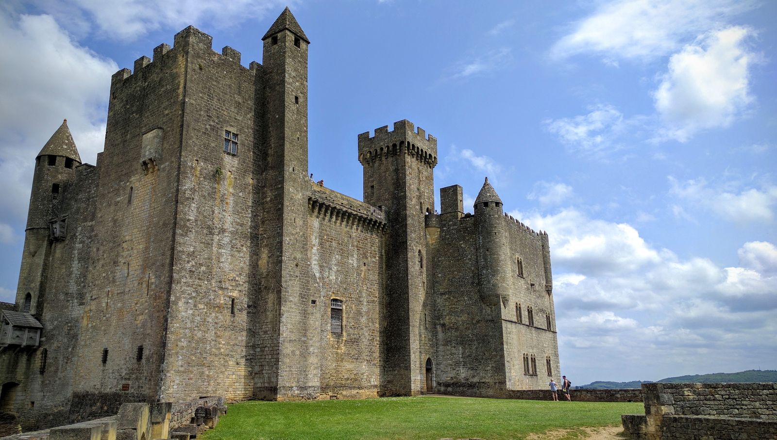 The tall square stone keep and towers of the Château de Beynac against a blue sky