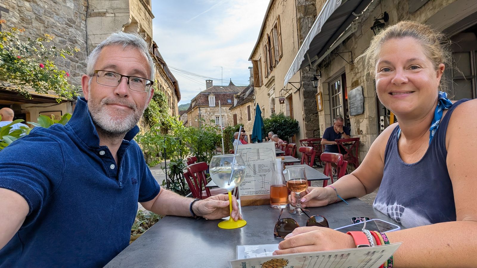 Kev and Cassie smiling at a café table in Carennac, with glasses of wine