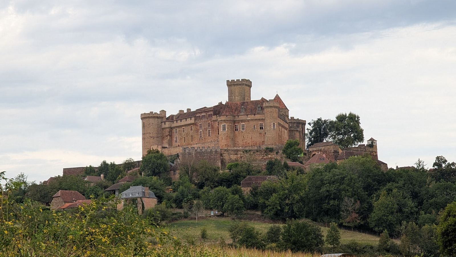 The Château de Castelnau-Bretenoux on a green hilltop above trees