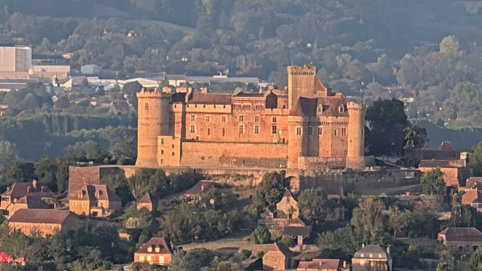 The red-gold walls and towers of the Château de Castelnau-Bretenoux above village roofs