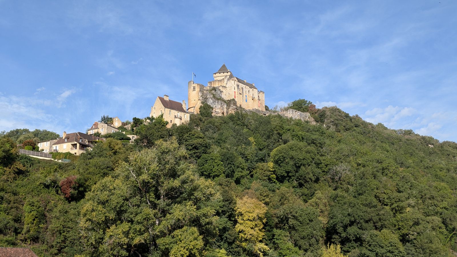 The Château de Castelnaud on a wooded hilltop under a blue sky