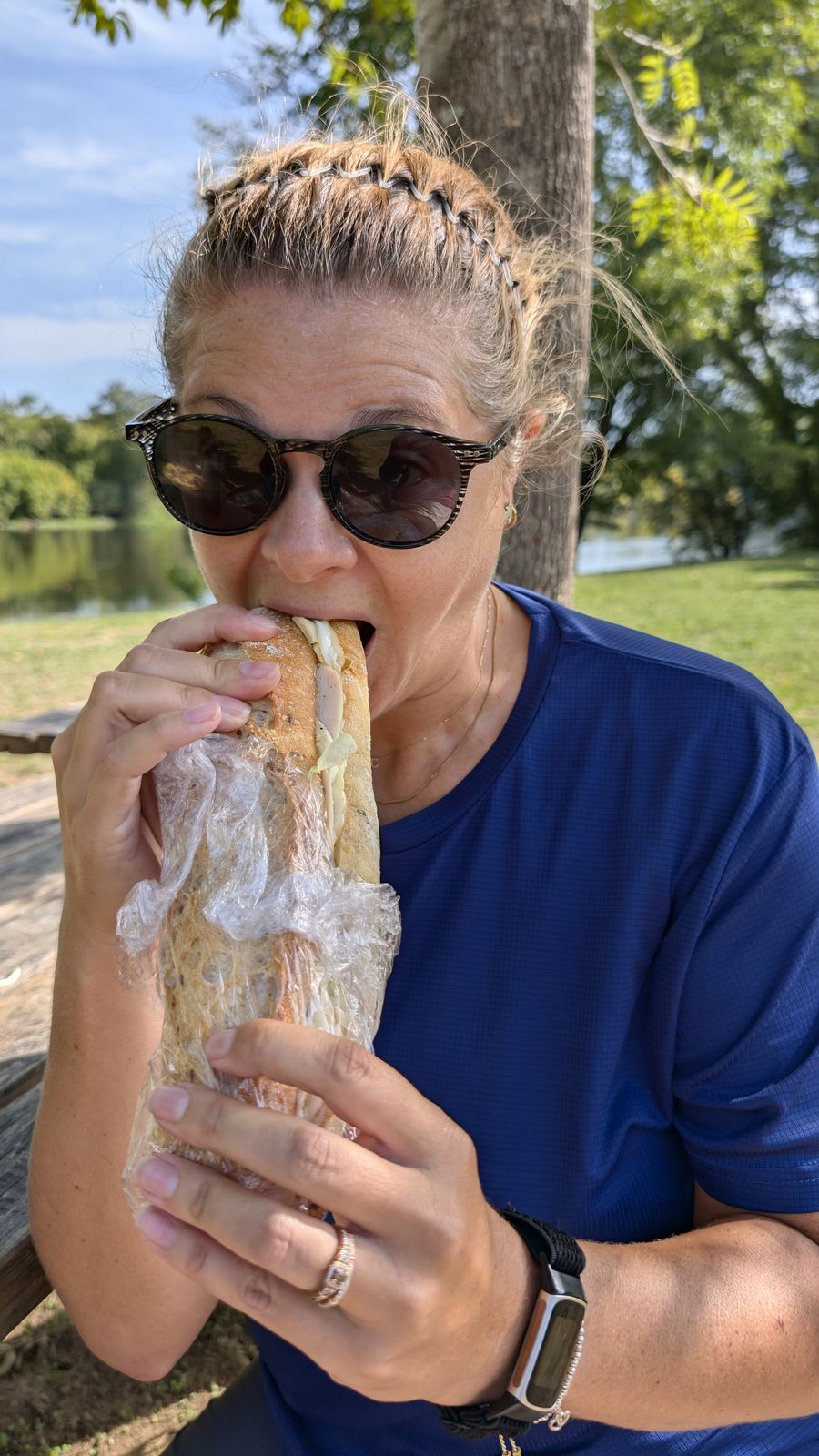 Cassie in sunglasses biting into a big baguette sandwich by the river at Castelnaud