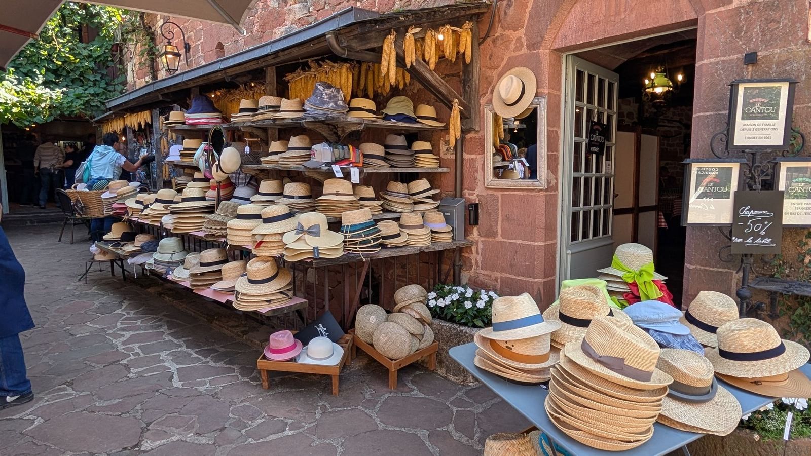 Rows of straw hats displayed outside a red sandstone shop in Collonges-la-Rouge