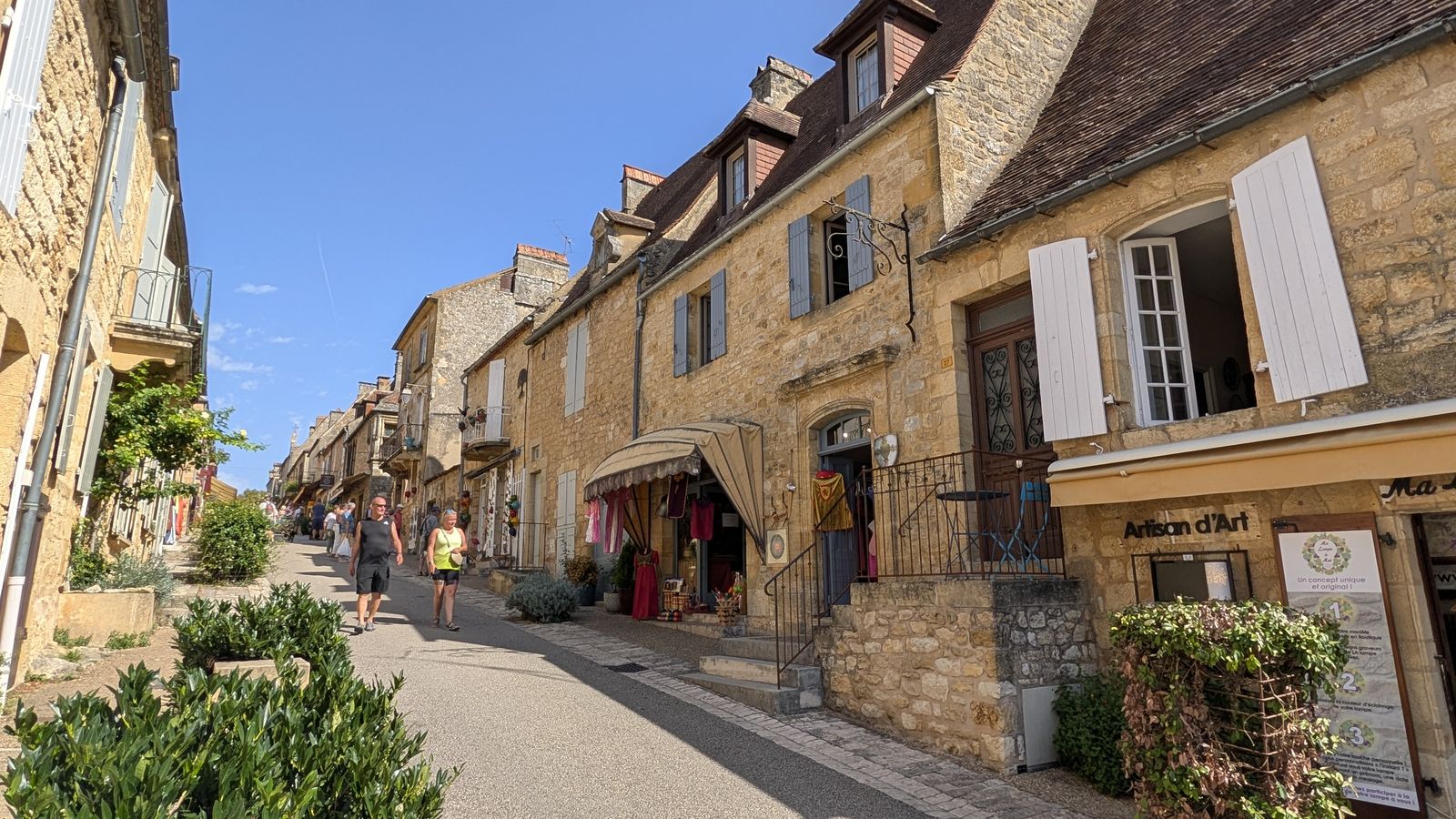 Golden-stone houses and shops along a sunny street in Domme