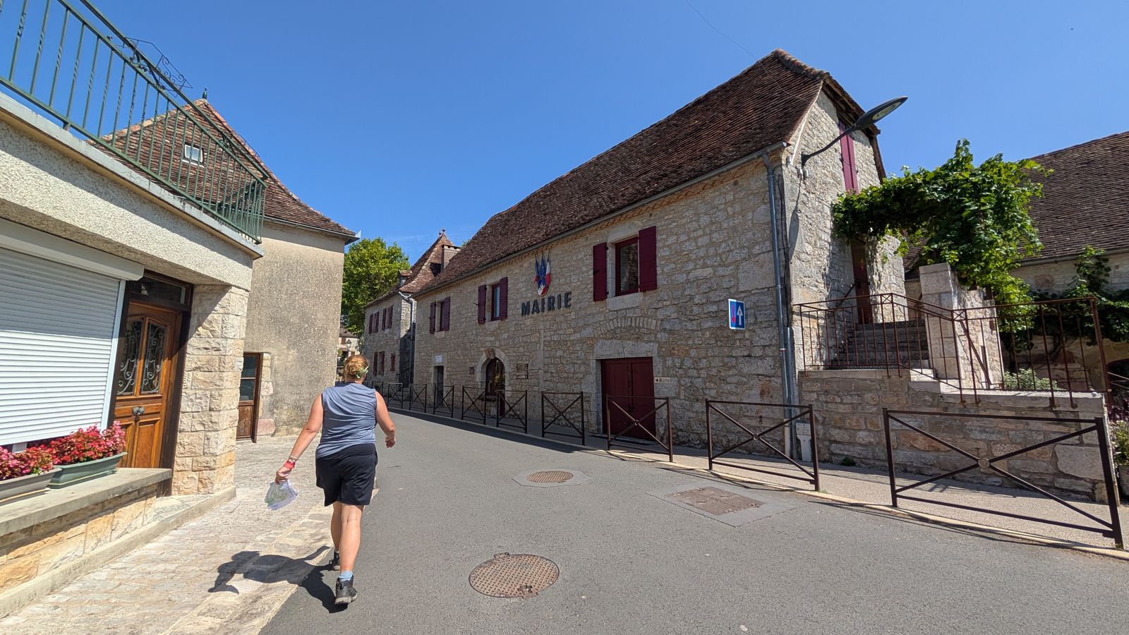 A walker on a village street between stone houses in Loubressac