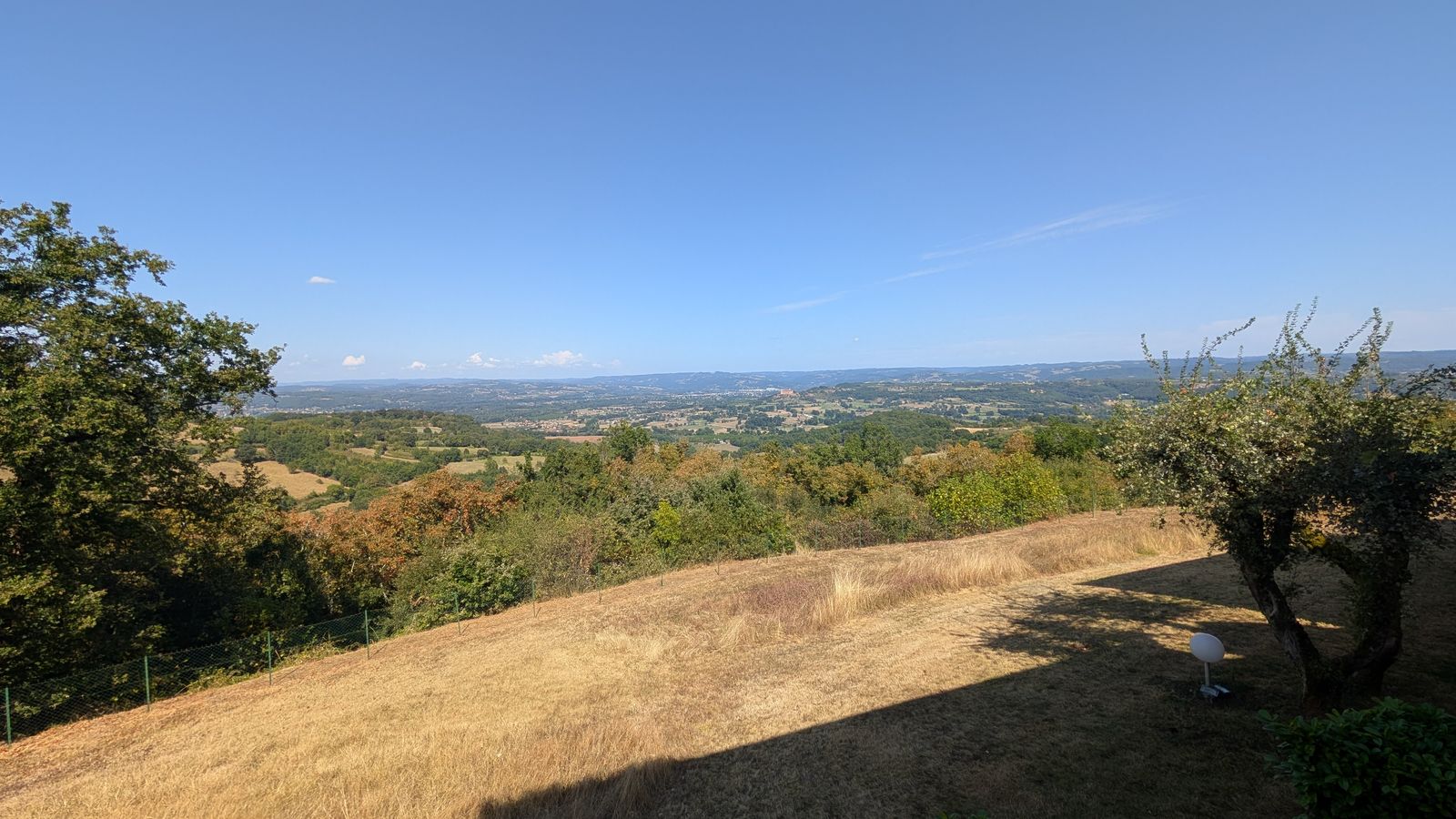 Sunlit grassland and wooded hills stretching away from the clifftop at Loubressac