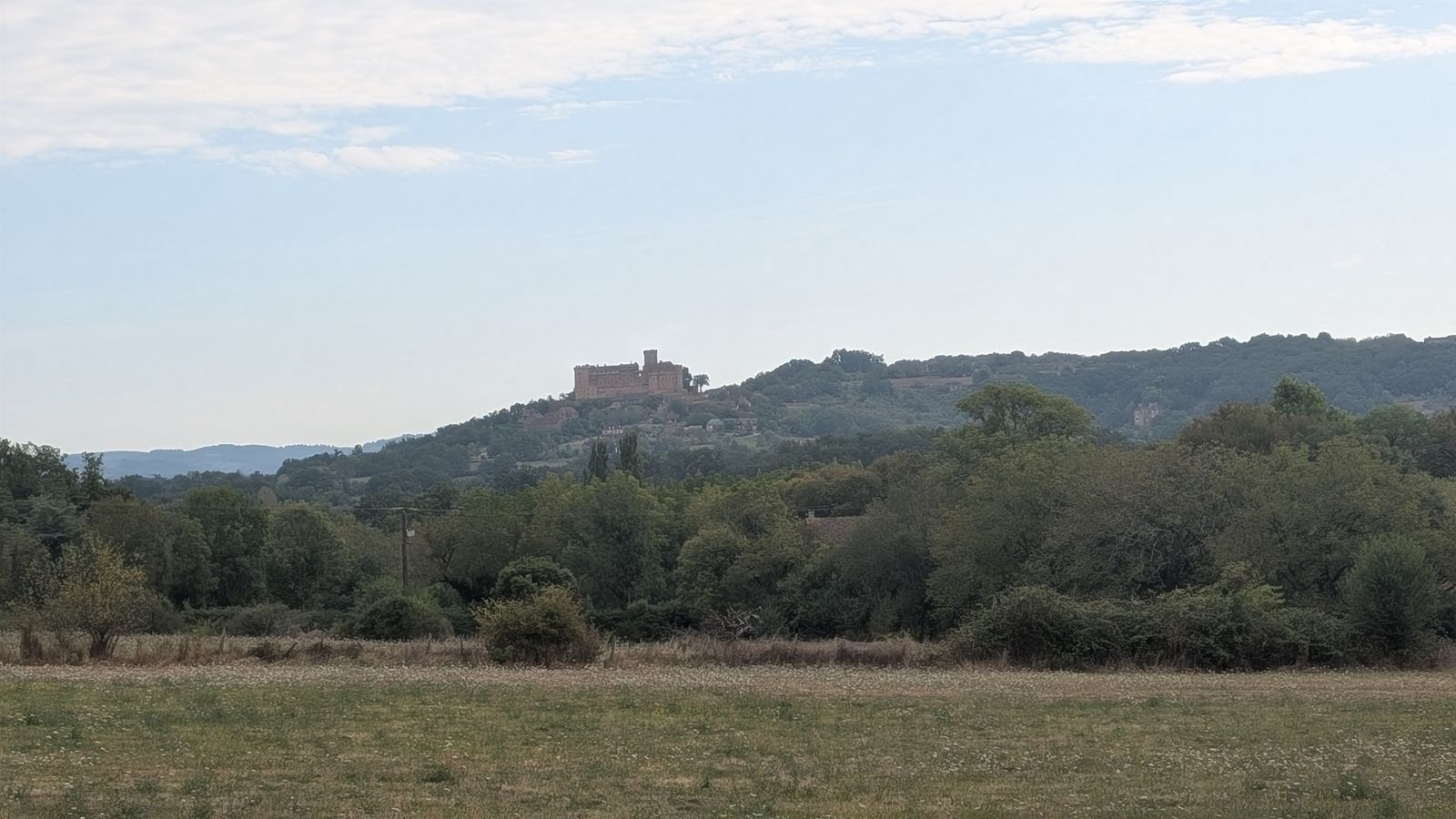 The Château de Castelnau-Bretenoux on a distant hilltop beyond a meadow and trees