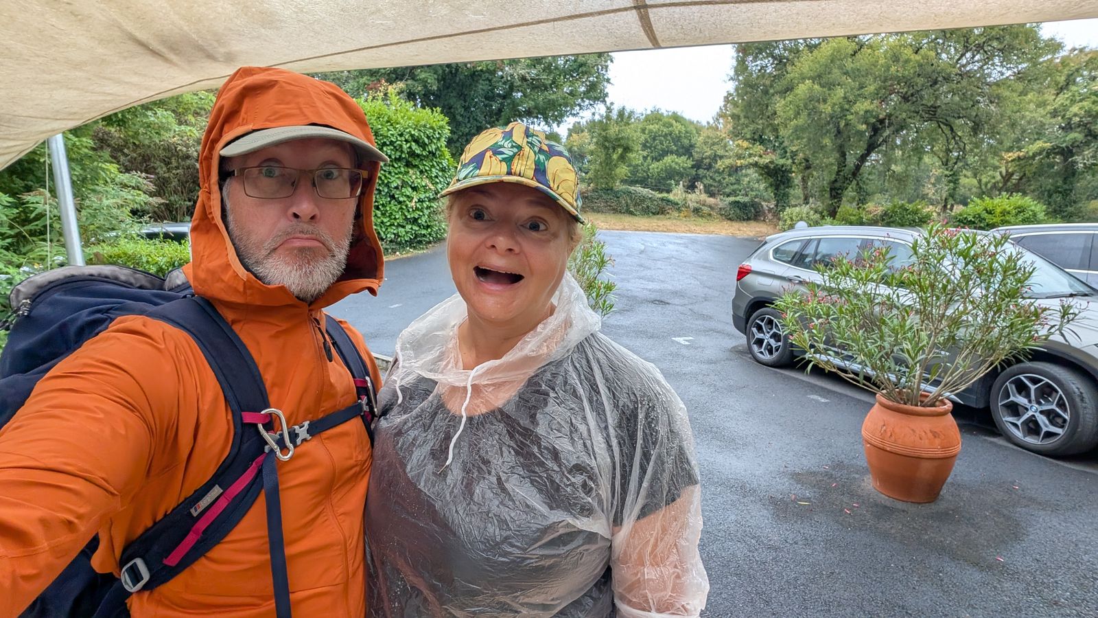 Kev in a rain jacket and Cassie in a plastic poncho grinning on a wet morning at Loubressac