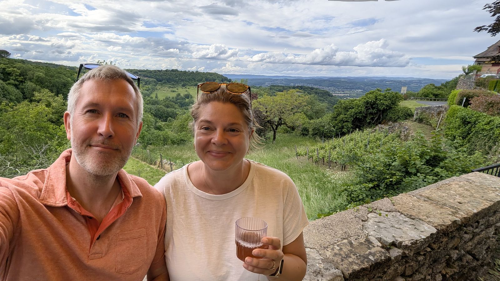 Cassie holding a glass of rosé on a terrace above the vineyards at Loubressac