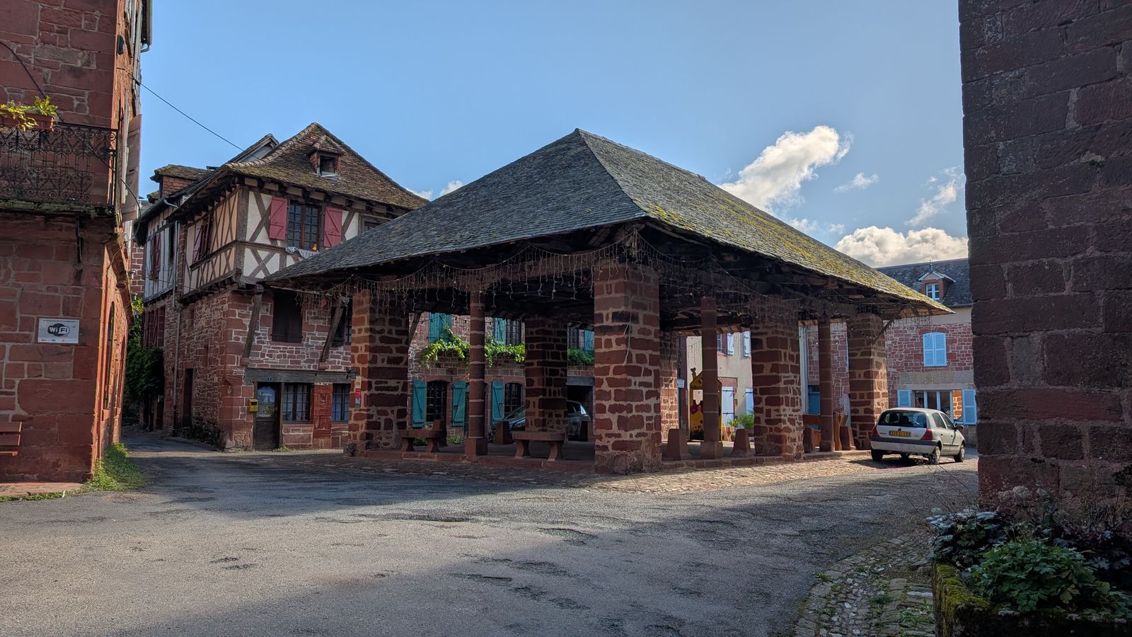 A red sandstone market hall with a tiled roof on a square in Meyssac