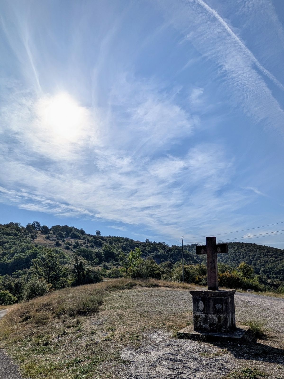 A stone cross on a plinth on open grassland under a bright sky near Rocamadour