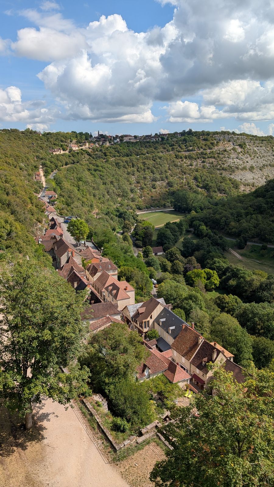 Rooftops and a road far below among trees, seen from the cliff at Rocamadour