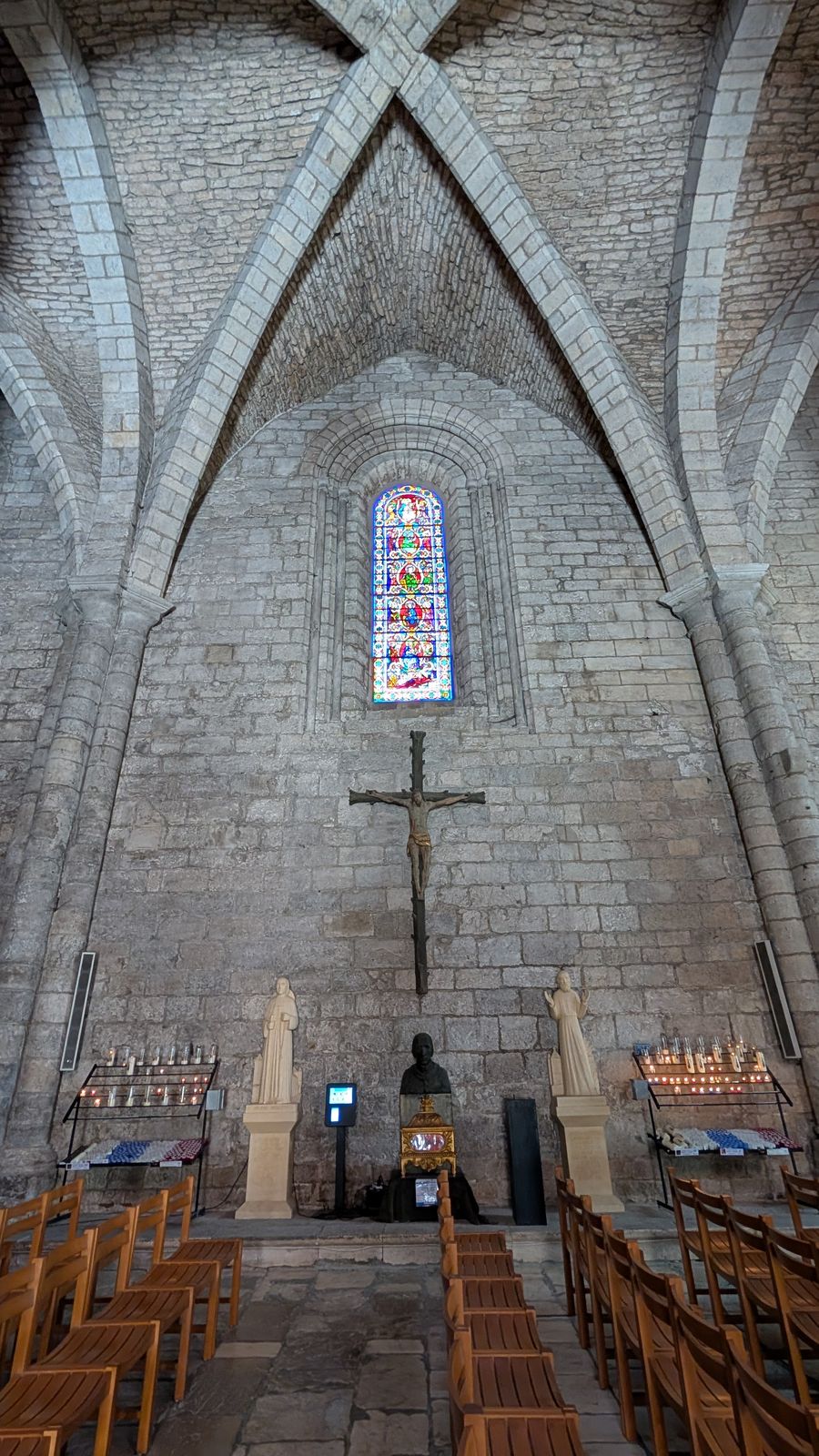A pale stone vaulted church interior with a wooden cross above the altar, Rocamadour
