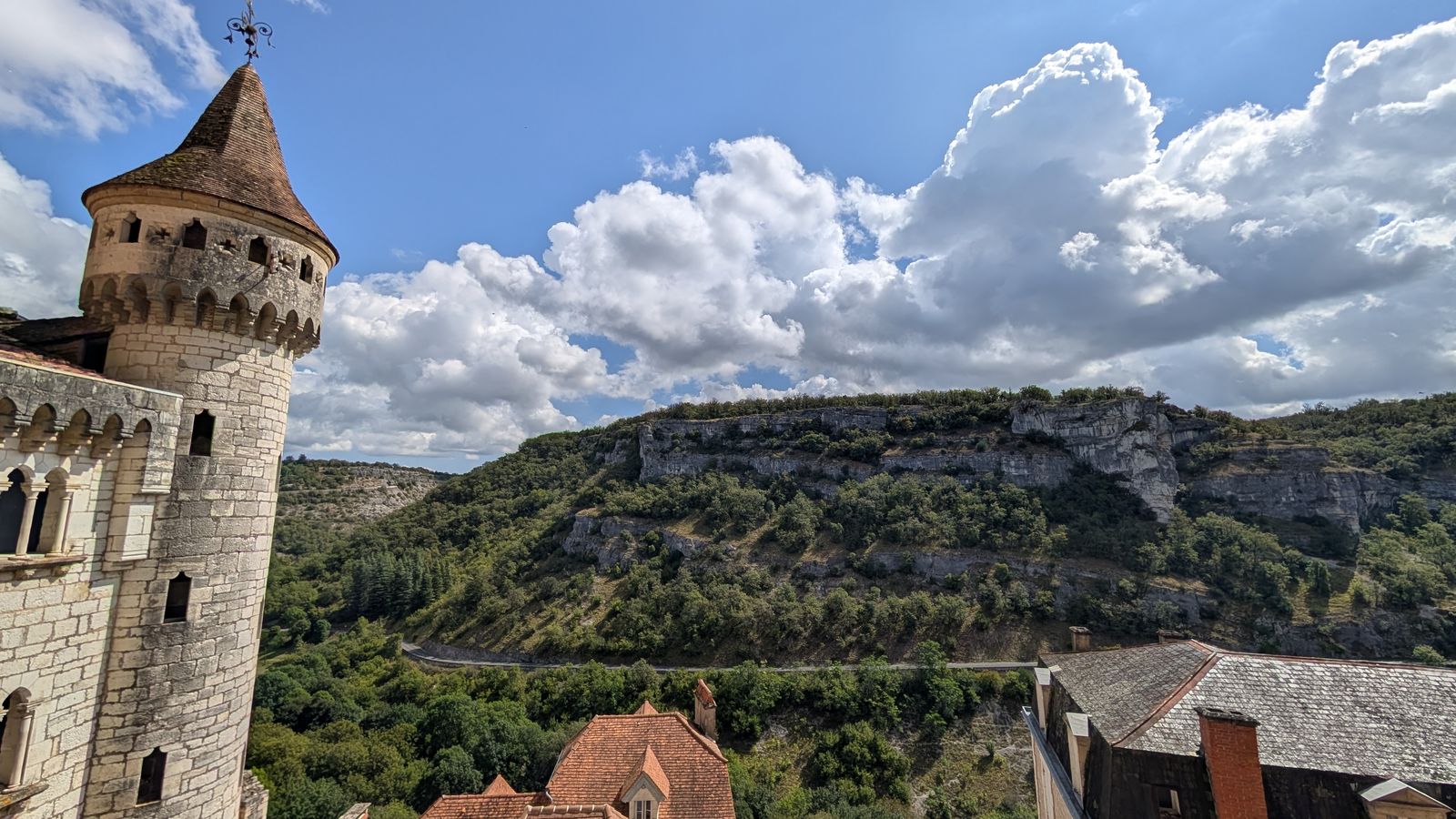 A round stone tower beside the cliff edge, with the wooded valley and cliffs beyond, Rocamadour