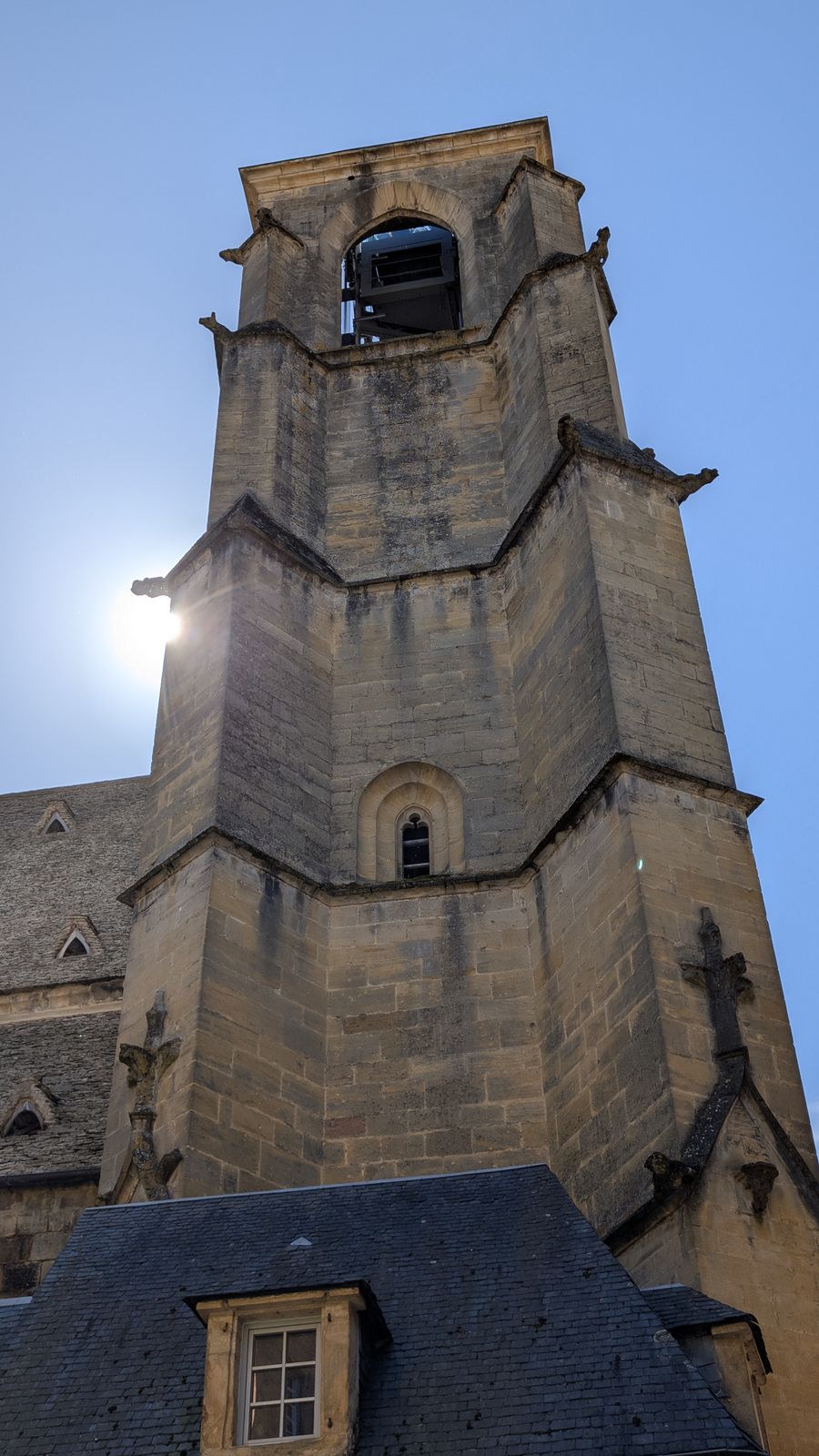 A tall square stone bell tower against a blue sky in Sarlat