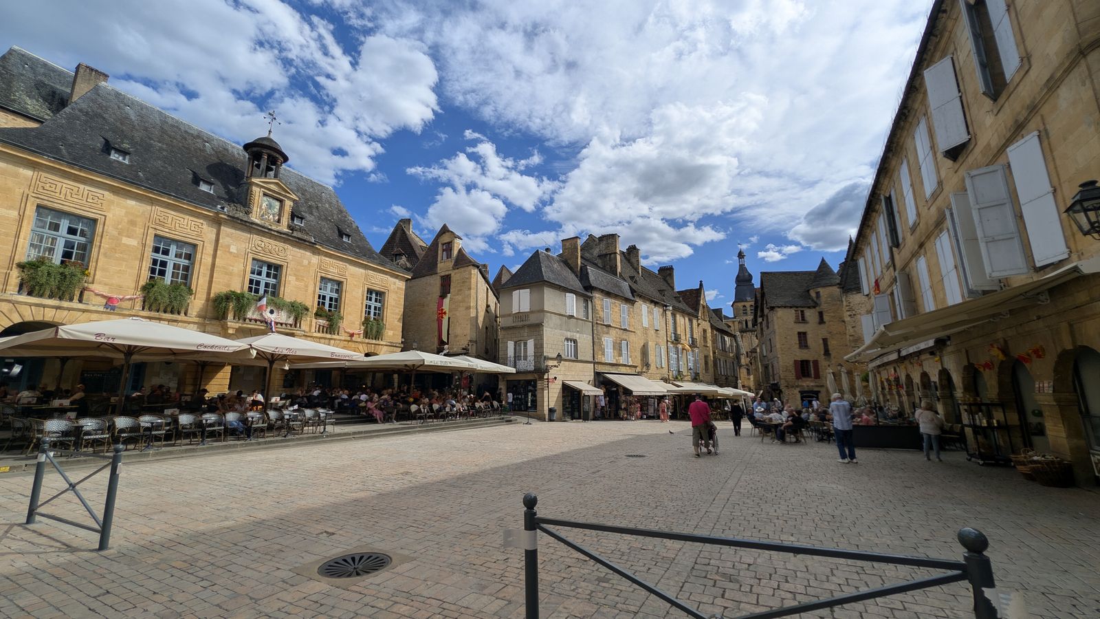 Café terraces and golden-stone houses around a sunny square in Sarlat
