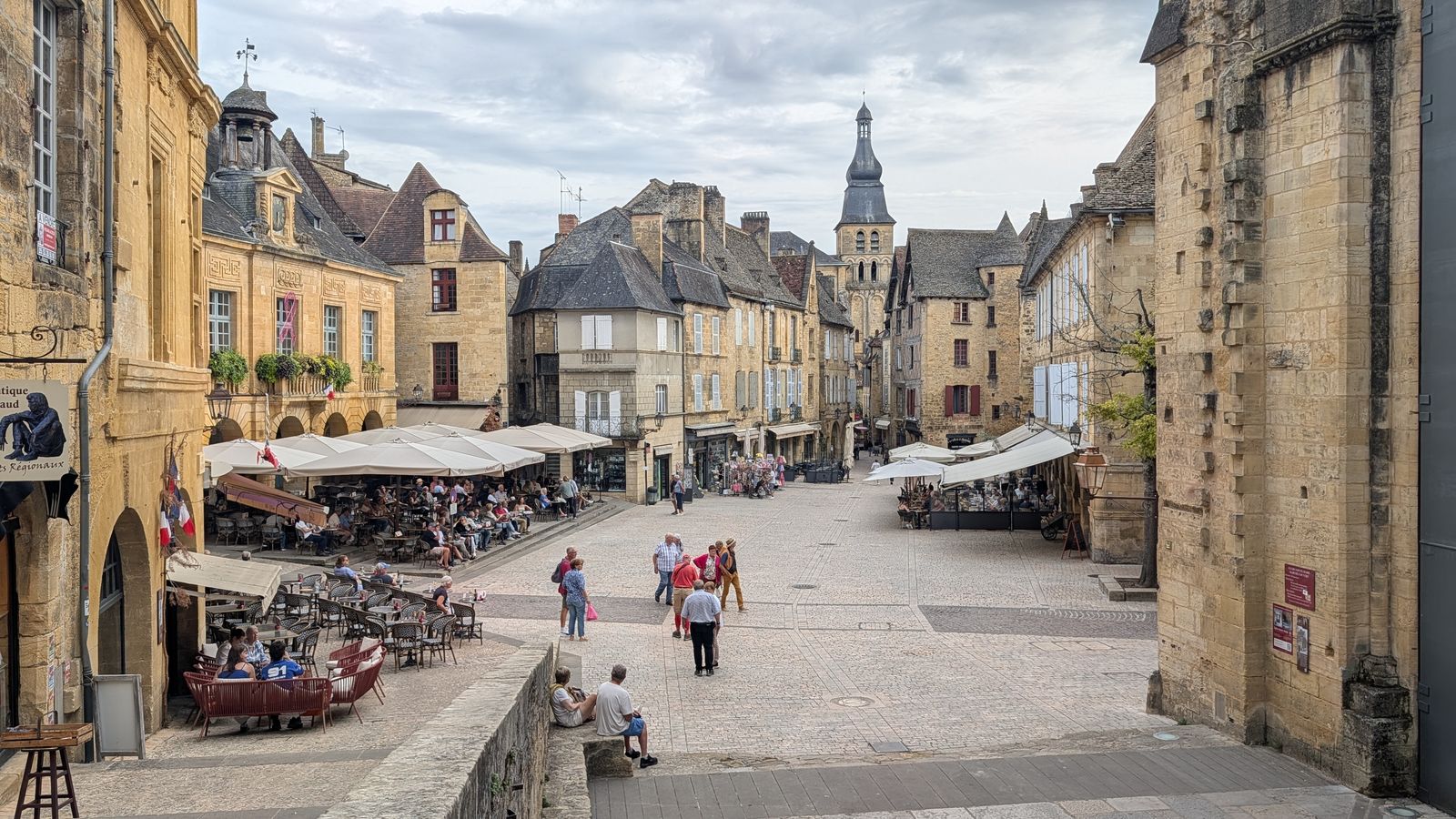 Café terraces and golden-stone houses on Place de la Liberté in Sarlat, seen from the steps above the square