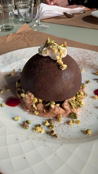 A chocolate dome dessert scattered with chopped pistachios