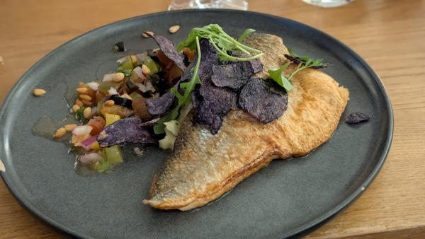 A pan-fried fish fillet topped with purple potato crisps and rocket