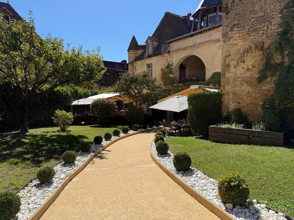 A gravel path between lawns and clipped box balls, leading to the terrace and stone walls of an old building