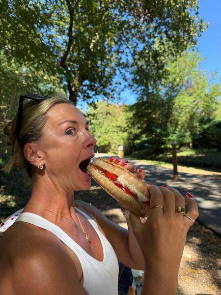 A guest taking a big bite of a baguette sandwich in the shade of the trees beside a path