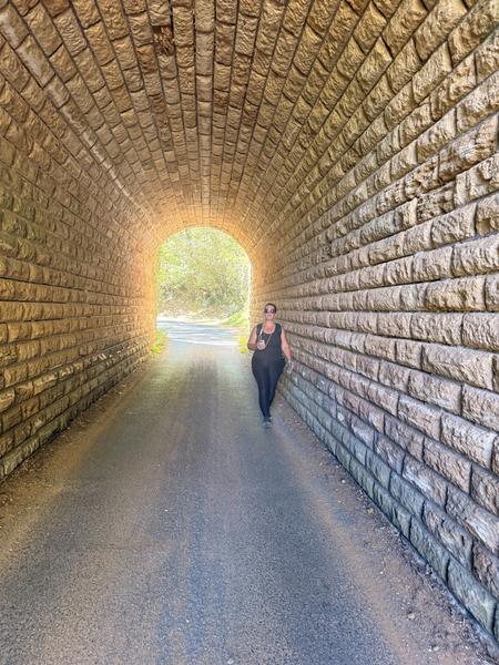 A walker in a long stone-lined tunnel, with sunlight at the far end