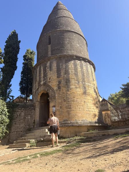 The conical stone tower of the Lanterne des Morts against a blue sky, with a visitor at its door