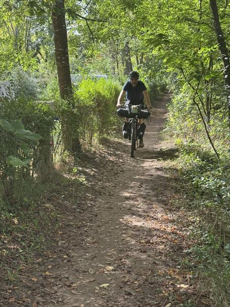 A cyclist with bike bags on a narrow woodland track near Castelnaud