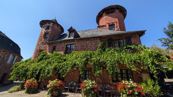 Red sandstone manor with round towers, ivy and red geraniums in Collonges-la-Rouge