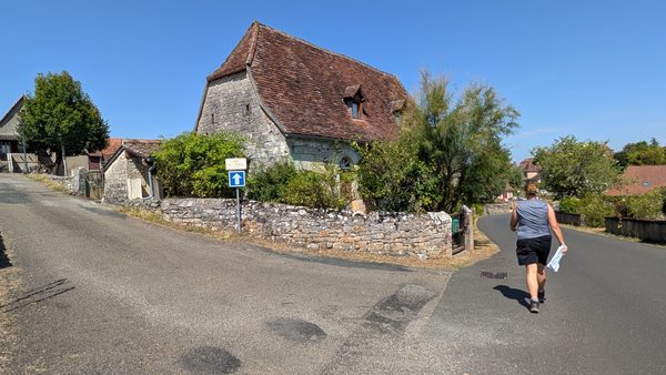 A walker with route notes in hand walking along a village street in Loubressac