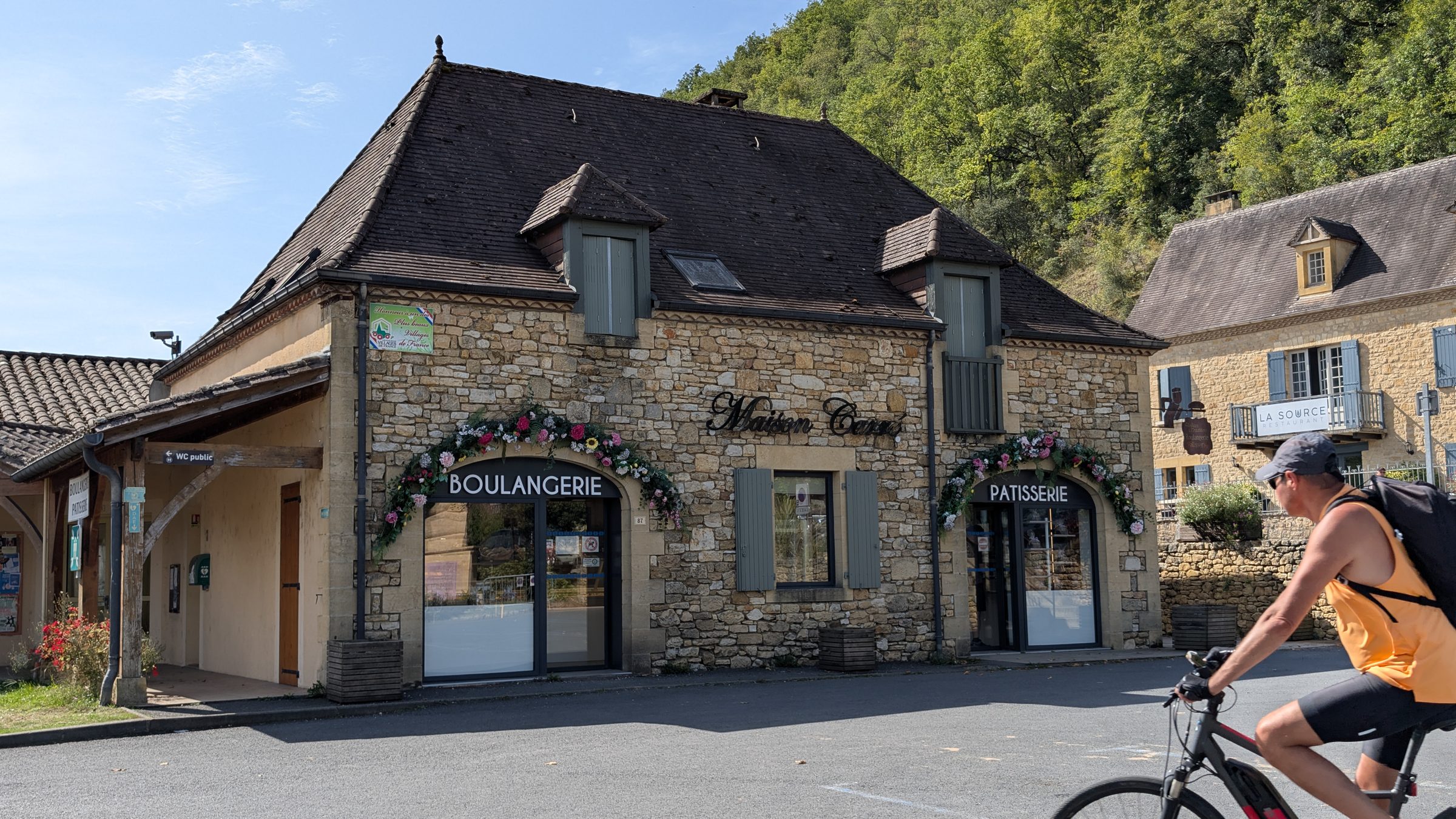 A cyclist on an e-bike passing a bakery in Castelnaud