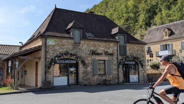 A cyclist on an e-bike passing a bakery in Castelnaud