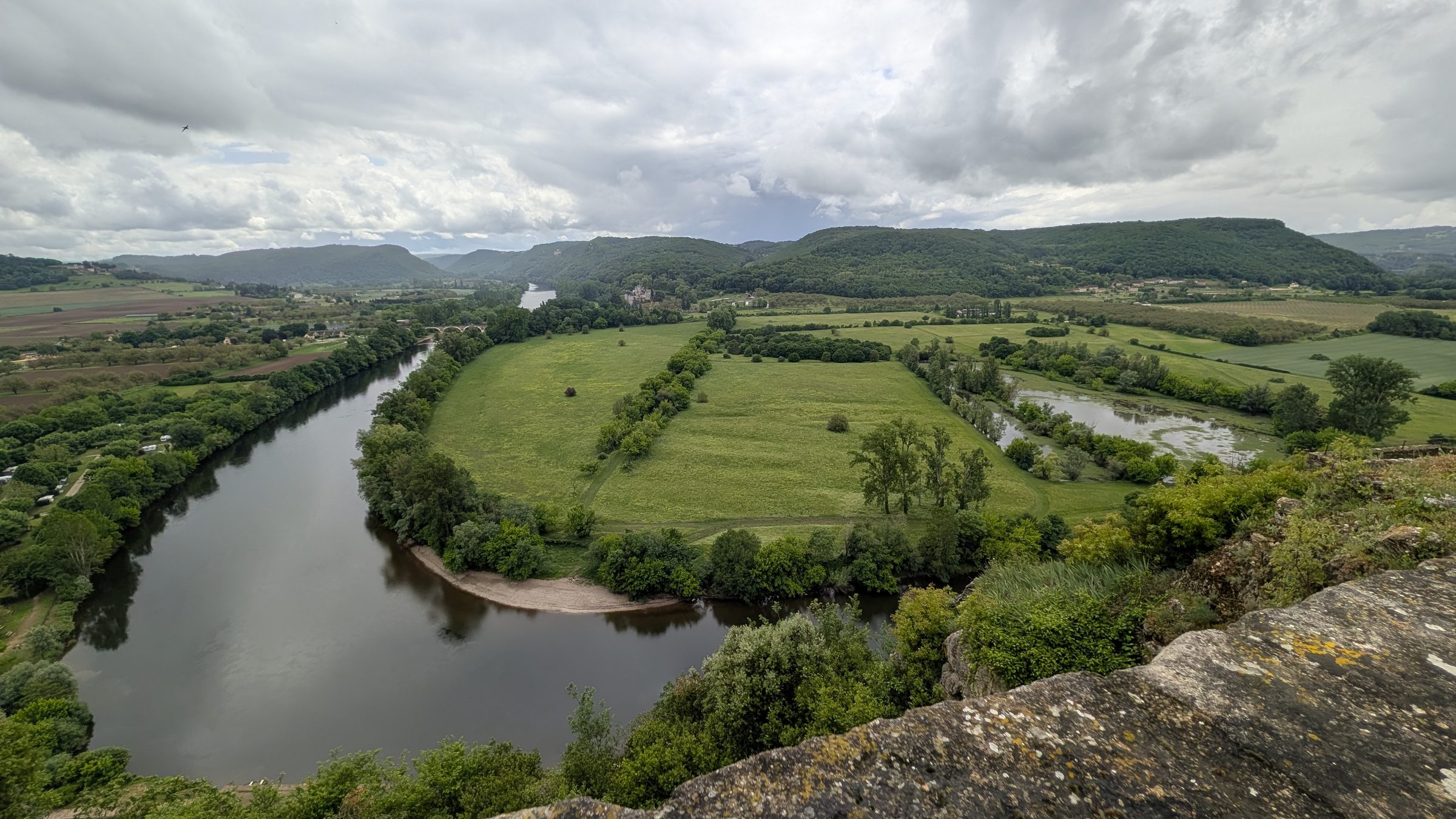 A loop of the Dordogne between green fields and woods, seen from high above at Beynac