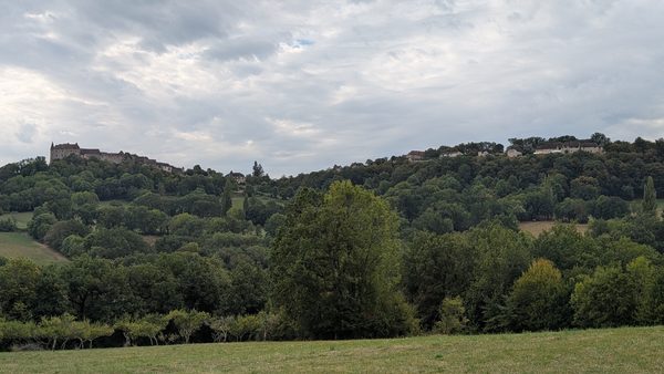 Green fields and wooded hills under a cloudy sky near Loubressac